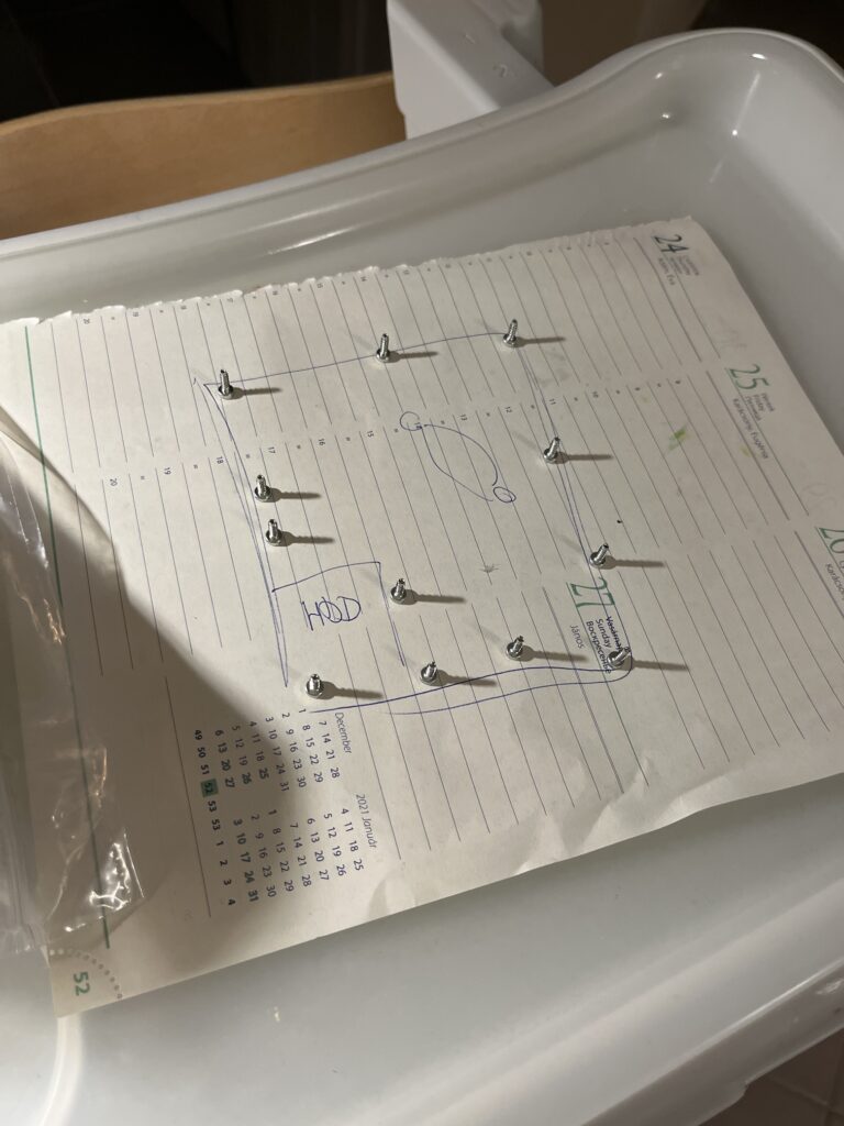 Papírlap egy sematikus ábrával, hogy a Play Station 4-ből kivett csavarok helyét szemléltesse.